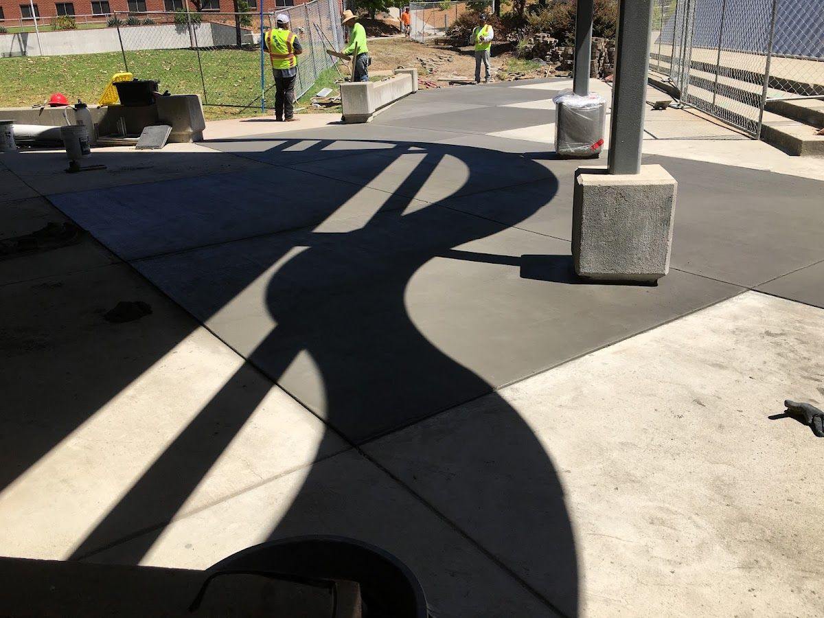 A broad finished concrete paved area jointed into bays, running past column bases in long afternoon shadow.