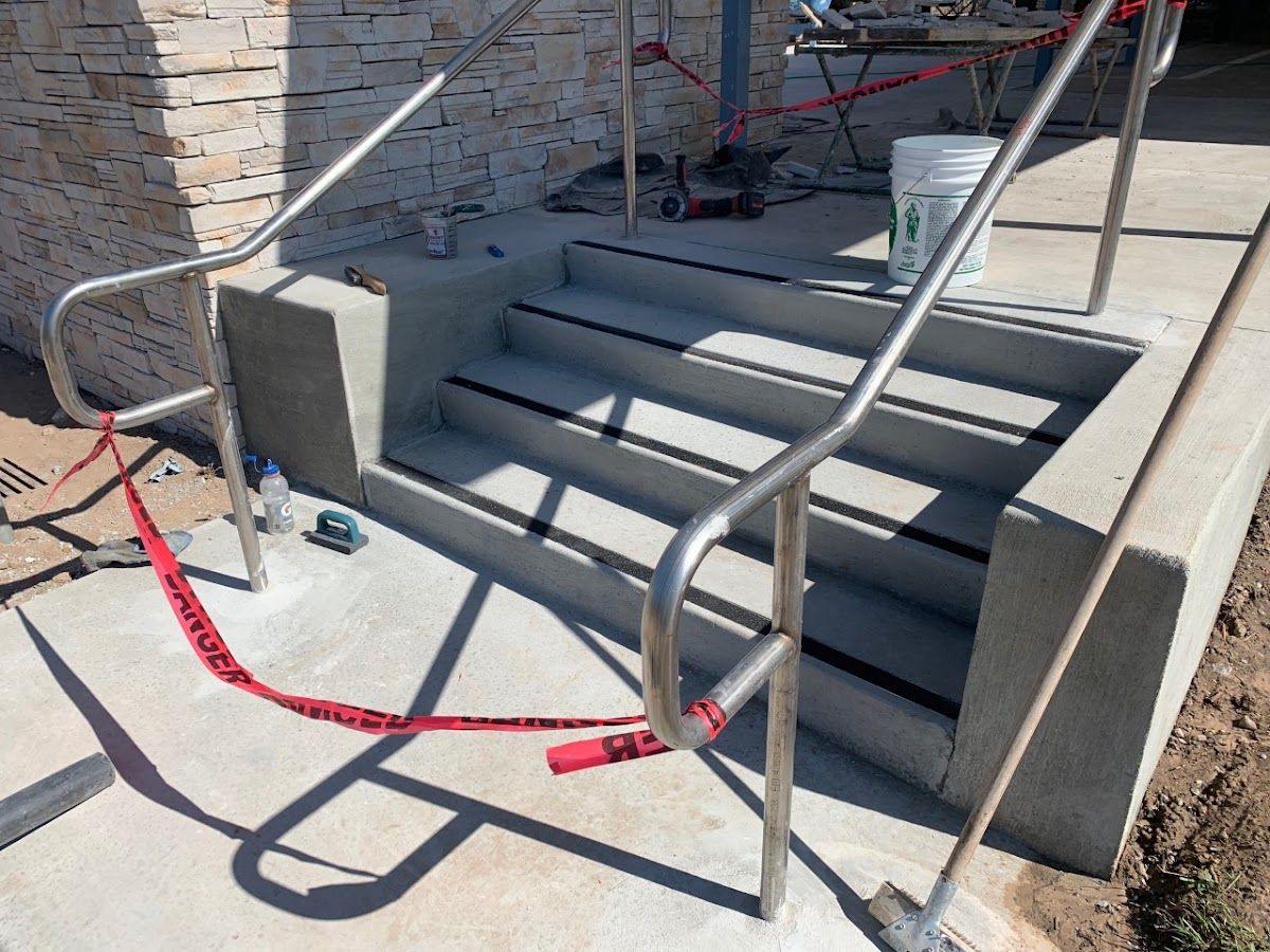 A cast concrete stair run against a stone-faced wall, with stainless handrails fitted on both sides.