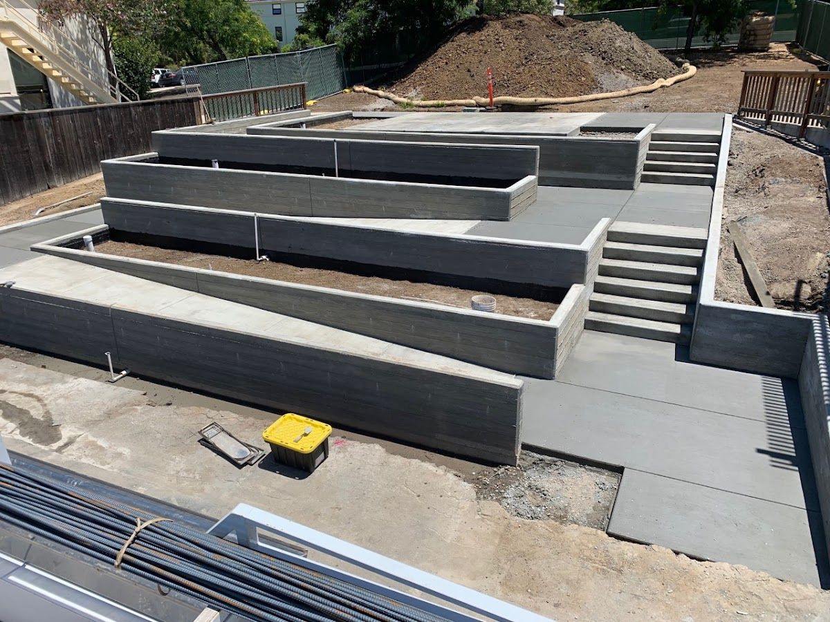 Poured concrete retaining walls stepping down a slope in tiers, with a cast stair run alongside.